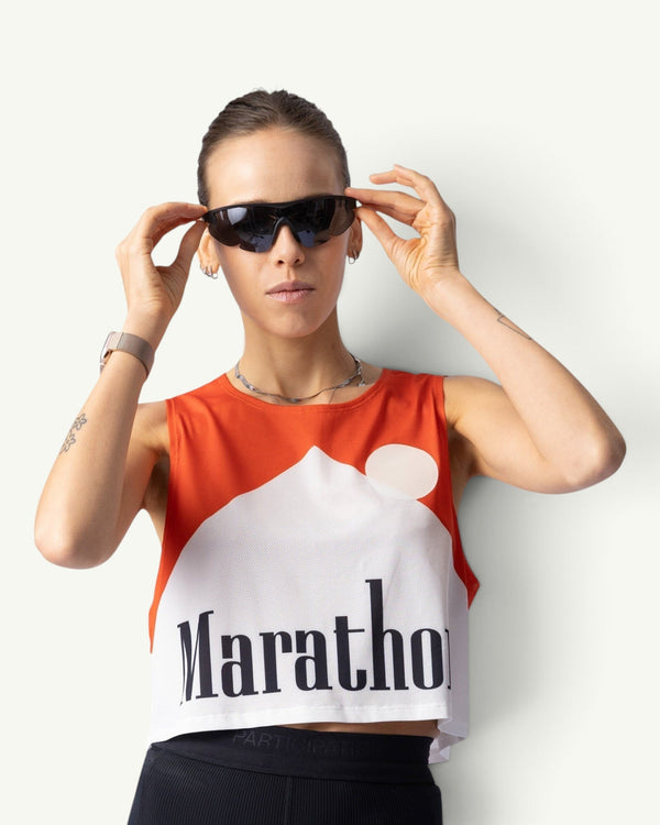 Participation Marathon red crop singlet with white graphic print worn by a woman adjusting black sports sunglasses
