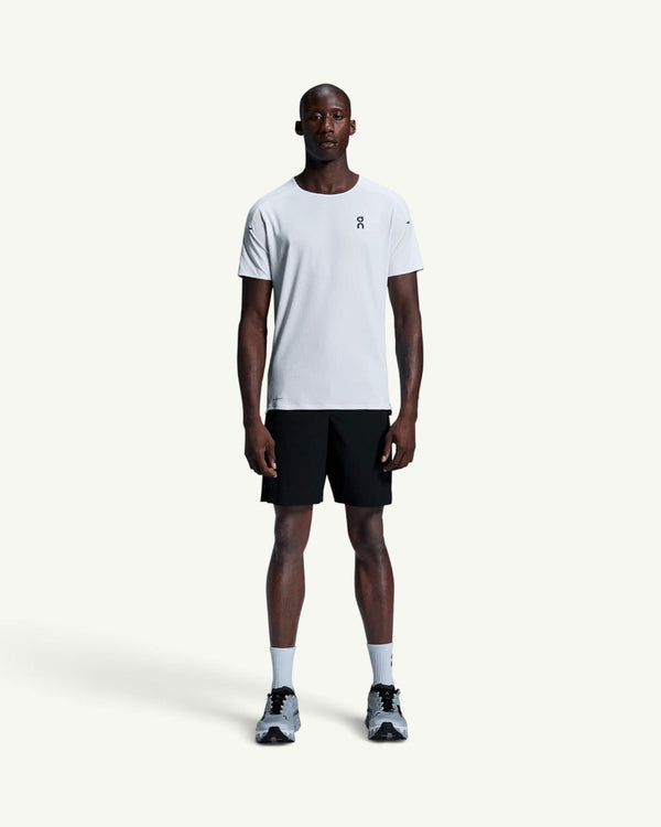 On men's white performance running t-shirt with athletic cut, worn by a model with black shorts and sneakers.