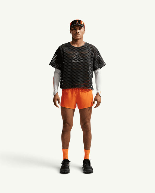 Nike ACG men's black open-hole mesh airflow short sleeve top worn with orange shorts and white arm sleeves