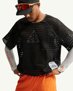 Nike ACG Men's Radical Airflow short sleeve top in black mesh, worn over grey sleeves and orange shorts.