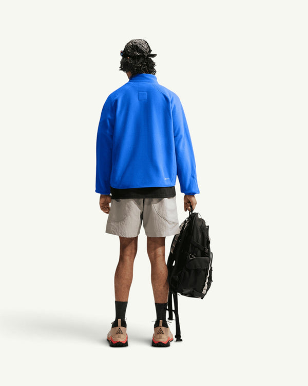 Nike ACG WOLF TREE FULL-ZIP JACKET in bright blue fleece worn by a model from the back with shorts and a backpack
