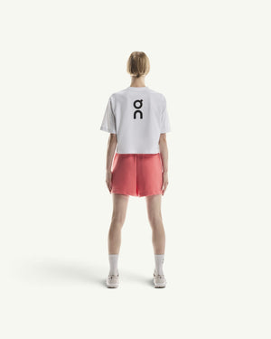 On women's white boxy cotton-blend t-shirt with black logo on back, paired with coral shorts, rear view