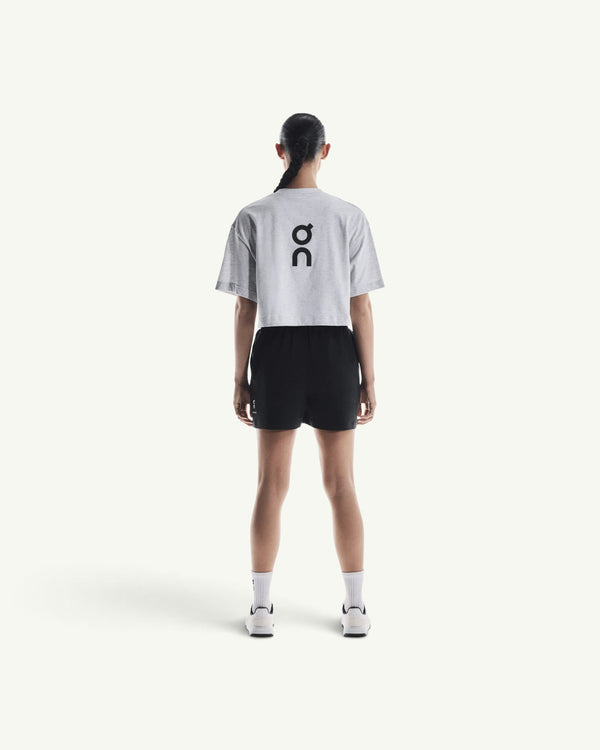 On women's grey boxy t-shirt with black logo on back, worn with black shorts and sneakers, rear view
