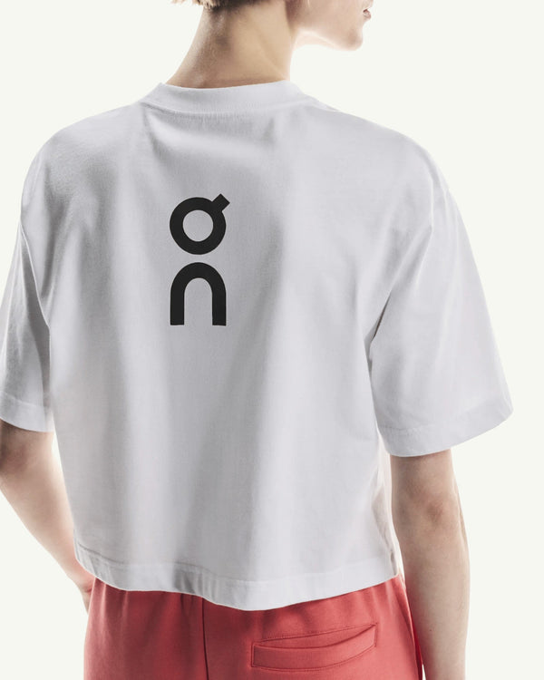 On women's white boxy t-shirt with a black logo on the back, worn with red shorts for a relaxed post-run look.