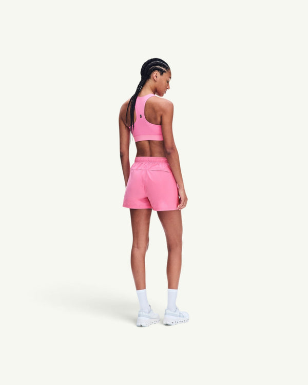 Model wearing an On pink racerback sports bra and matching athletic shorts, viewed from the back.