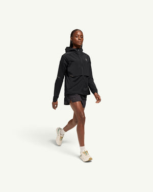 On women's black lightweight hooded windbreaker jacket worn by a runner with matching shorts and sneakers