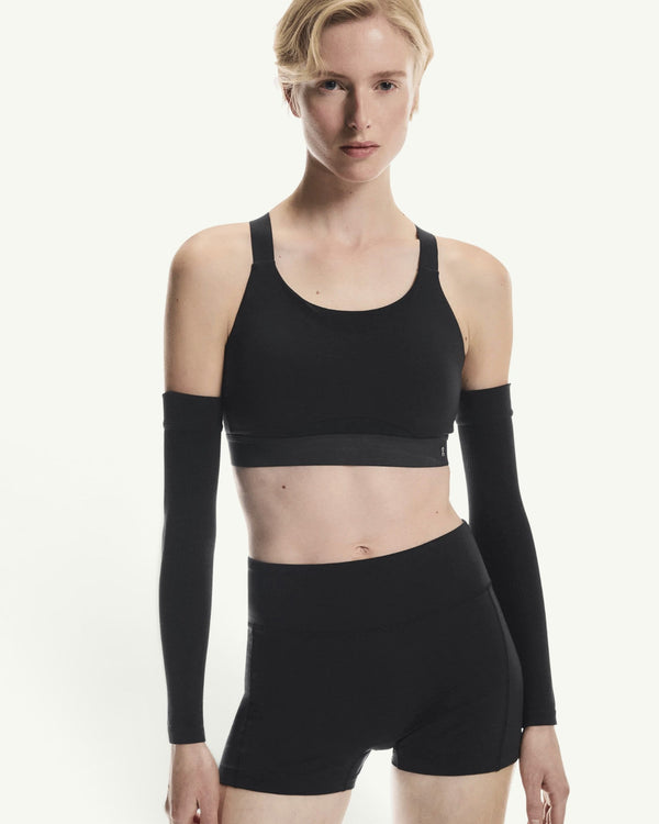 On model wearing a black performance sports bra with matching arm sleeves and leggings for high-intensity training