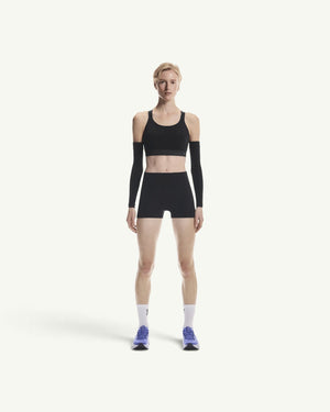 On model wearing a black performance sports bra and matching shorts with arm sleeves for a secure athletic fit.