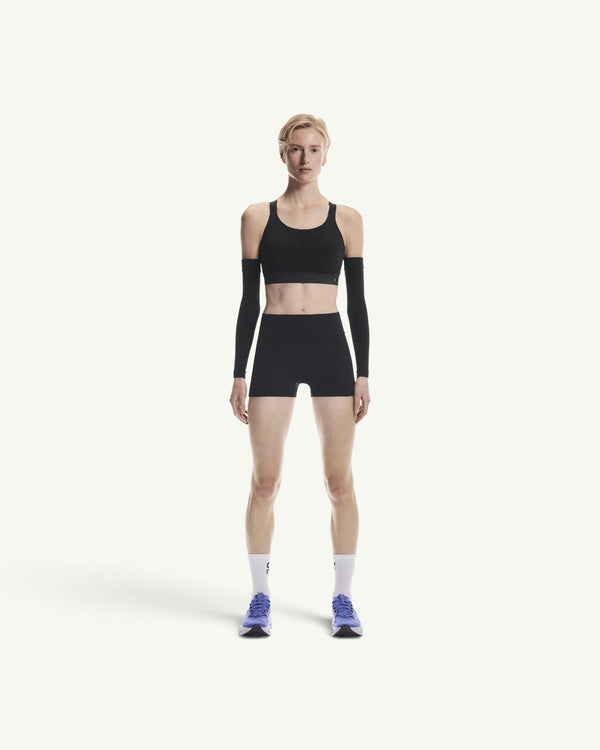 On model wearing a black performance sports bra and matching shorts with arm sleeves for a secure athletic fit.