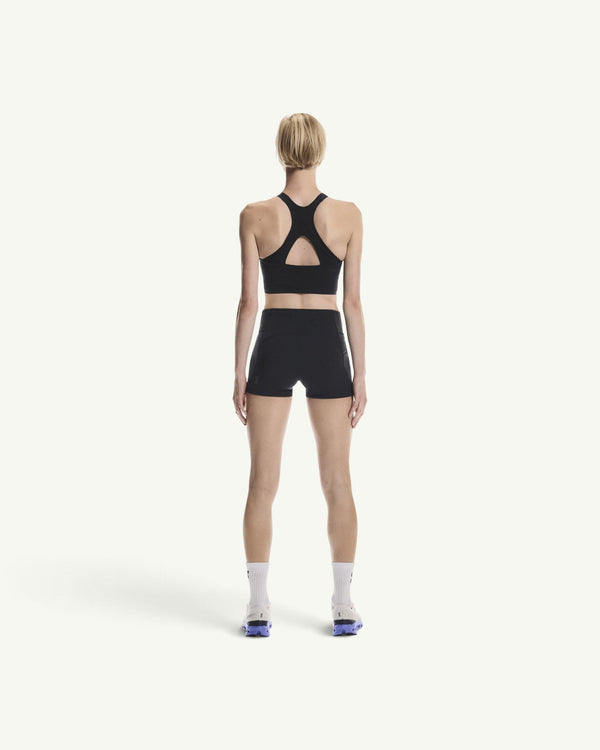 Back view of a woman wearing an On black performance crop top and matching shorts for running