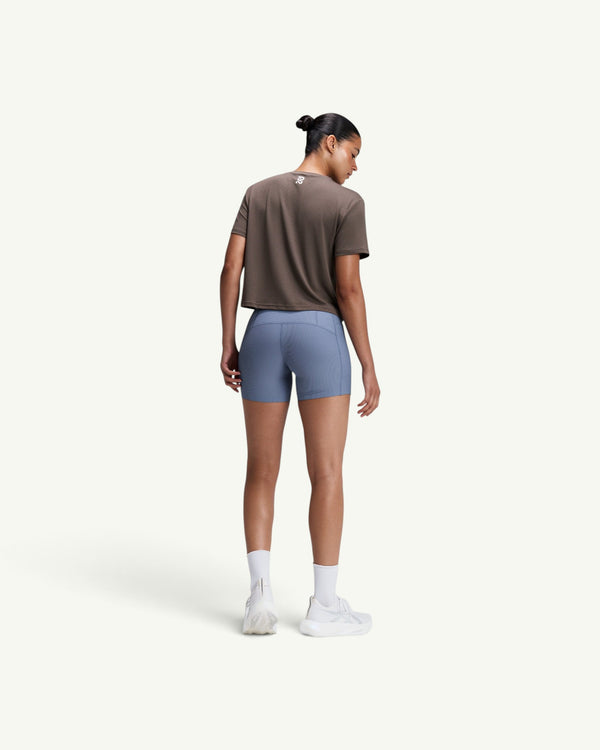 Amateur women's brown micromesh cropped run tee with reflective branding, worn with blue athletic shorts from behind.