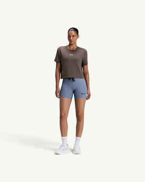 Amateur model wearing a brown Micromesh cropped run tee with a crew neck and reflective branding, paired with blue shorts.