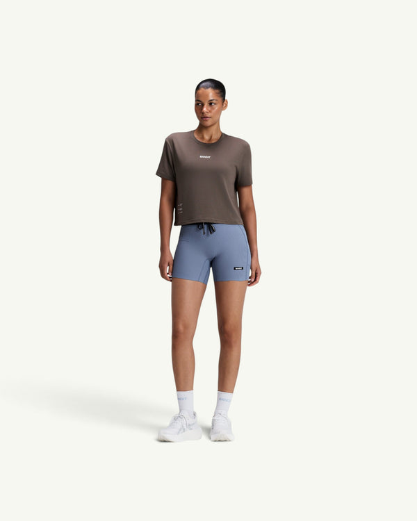 Amateur model wearing a brown Micromesh cropped run tee with a crew neck and reflective branding, paired with blue shorts.