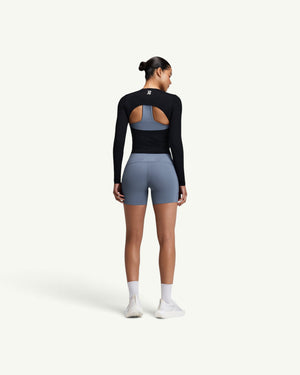 Amateur women's black GeoMesh long sleeve top with a half-moon back cutout, worn over a blue sports bra and shorts.