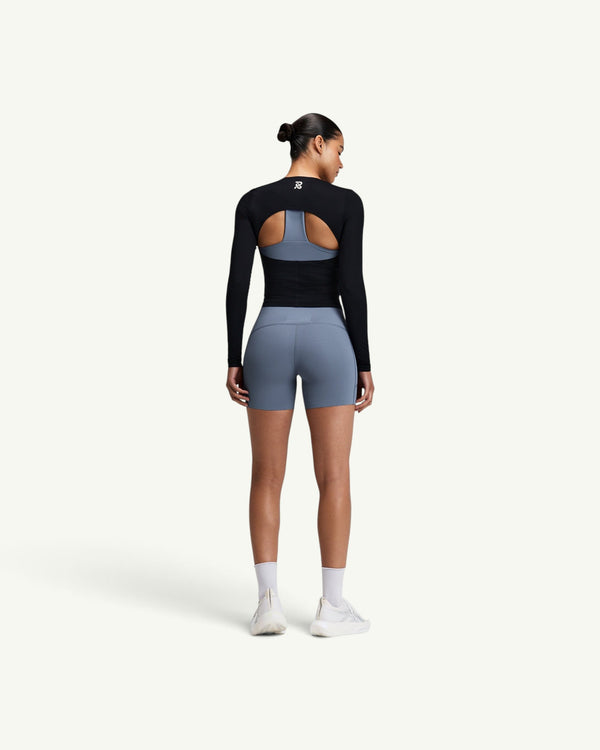 Amateur women's black GeoMesh long sleeve top with a half-moon back cutout, worn over a blue sports bra and shorts.