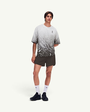 Amateur model wearing dark grey performance shorts and a patterned grey t-shirt with white socks and black sneakers