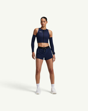 Amateur women's navy blue Adapto 2-way zip race crop top with matching arm sleeves and running shorts