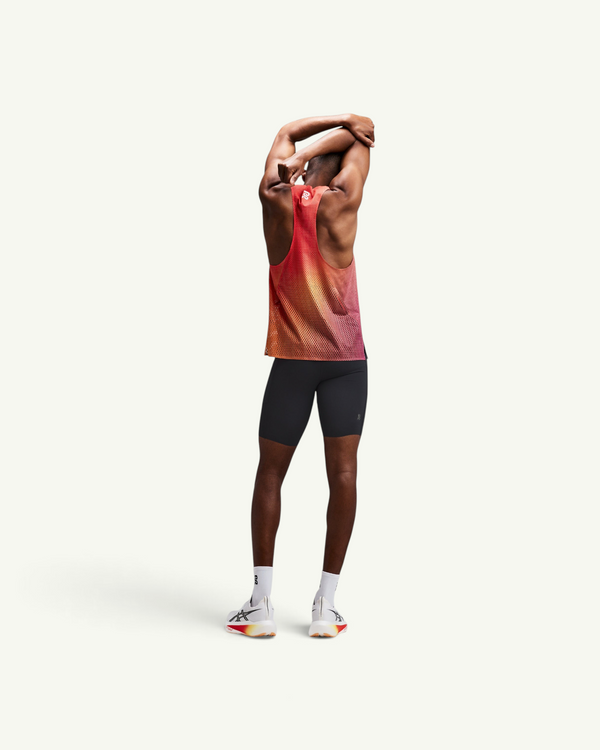 Amateur men's black compression half tights worn by a runner stretching in a red and orange mesh tank top