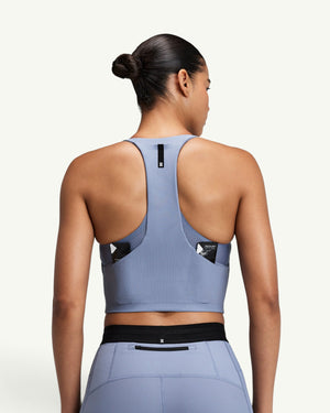 Amateur women's blue ribbed T-back race crop top with back storage pockets, worn by a model from a rear view.