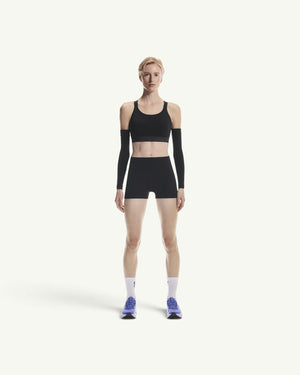 Amateur women's black 3-inch performance running tights worn by a model with a matching sports bra and arm sleeves