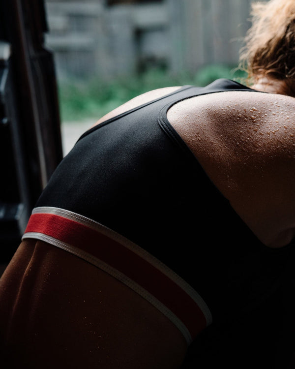 Amateur women's black racerback running bra with red and white striped band, worn by a runner with sweaty skin.