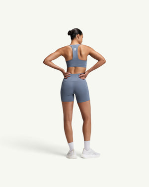 Amateur women's high-waist compression shorts in blue with side pockets and grip hem, worn by a model from the back.