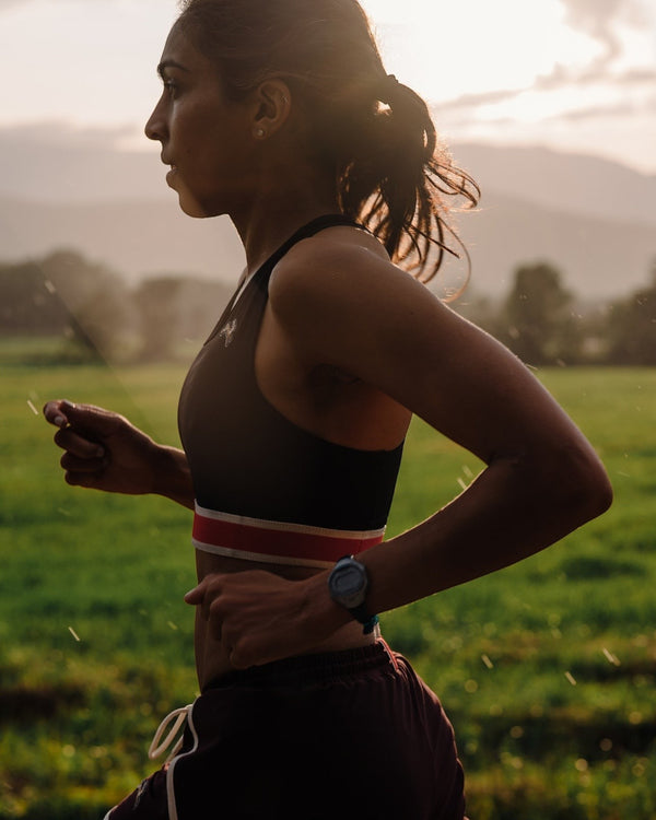 Amateur women's medium-impact racerback running bra in black with a red and white band, worn by a runner outdoors.