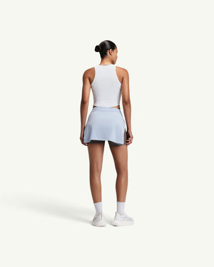 Amateur women's white ribbed performance tank top worn by a model from the back view with a light blue skirt.